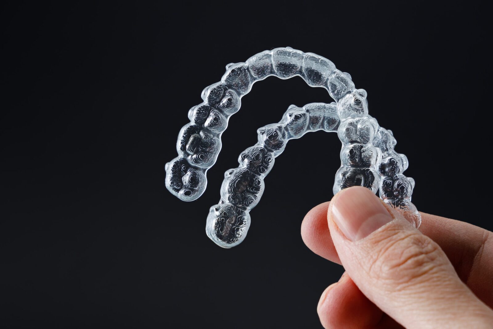 hand-holding-two-transparent-retainers-on-black-background-invisalign-orthodontics-concept-1600x1066 (1)